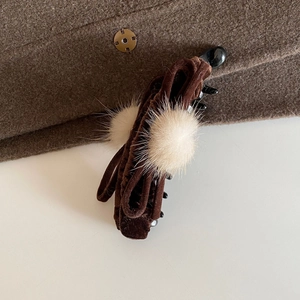 Detail of velvet bow banana clip with fuzzy pom-poms on premium wool fabric