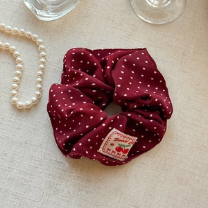 Detailansicht von weinrot gepunktetem Scrunchie mit Kirsche-Etikett auf Leinenstoff
