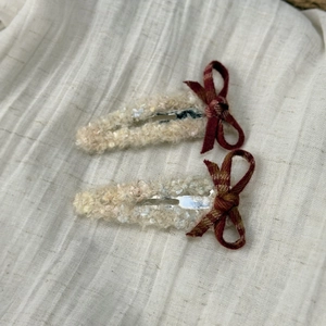 Detail of plush cream fabric hair clips with red plaid bow accents and soft texture