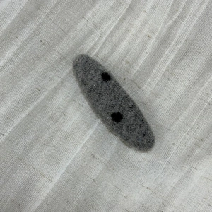 Detail of gray felt hair clip featuring minimalist black polka dots on soft fabric