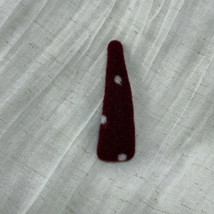 Detailed close-up of dark red felt hair clip with white polka dots on linen texture