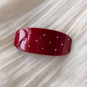 Detail einer dunkelroten Haarspange mit funkelnden Strasssteinen auf beigem Stoff