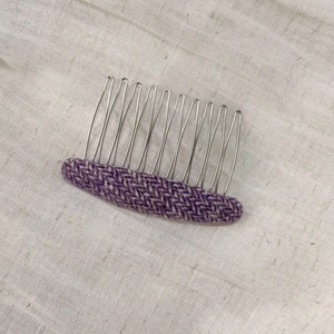 Close-up of purple herringbone fabric hair comb with ten silver metal teeth on linen