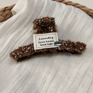 Detailed close-up of a brown plush shark hair clip with a vintage cloth label and metal charm