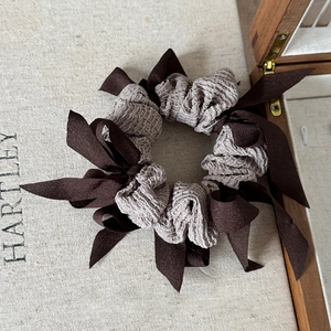 Detailed view of large taupe scrunchie with dark brown ribbons on a wooden box