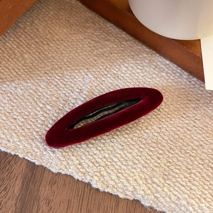 Vintage burgundy velvet oval hair clip with hollow design on minimalist woven background