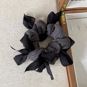 Elegant black woven bow scrunchie for women with layered chiffon ribbons on beige fabric