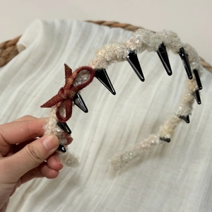 Detail view of beige plush headband featuring inner black teeth and a red plaid bow accent