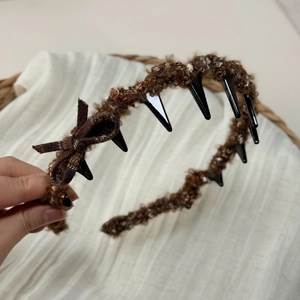 Close-up of brown bouclé headband featuring a plaid bow and inner plastic teeth