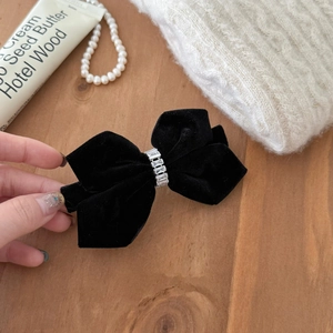 Detailed close-up of a black velvet bow hair clip with crystal rhinestones on wood