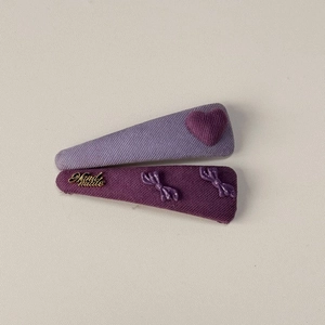 Détail de pinces à cheveux en tissu violet avec motif de cœur, nœuds et étiquette en métal