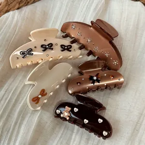 Maillard brown hair claws with rhinestones and black bows on white textured fabric