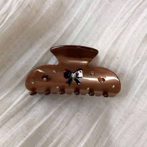 Detail shot of brown acetate shark clip with rhinestone bow on beige fabric