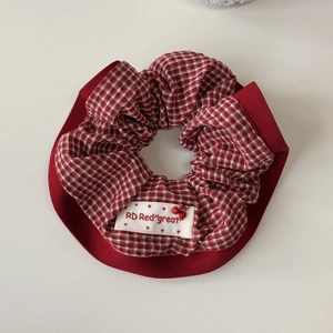 Dettaglio di scrunchie a quadretti rossi con etichetta logo e ciondoli ciliegia