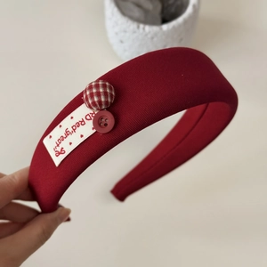 Dettaglio del cerchietto in tessuto rosso con bottone a quadri e toppa vintage
