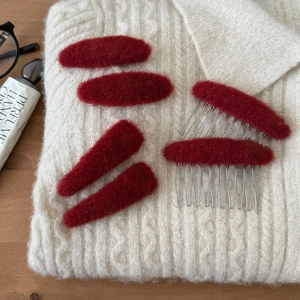 Detailansicht von roten Plüsch-Haarspangen und Kamm-Set auf strukturiertem weißem Pullover