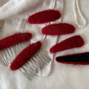 Set aus roten Plüsch-Haarklammern und Kämmen auf edlem Stoffhintergrund für Winter-Styling