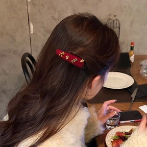 Dettaglio del fermaglio per capelli in peluche rosso con ciondoli dorati indossato di lato