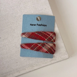 Close-up of red plaid fabric BB hair clips on display card with warm winter texture