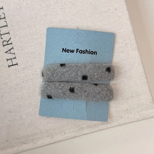 Set of two gray felt hair clips with black polka dots on a blue fashion display card