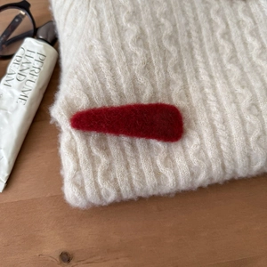 Nahaufnahme einer roten Plüsch-Haarklammer auf einem weißen grob gestrickten Pullover