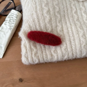 Detailansicht einer roten Plüsch-Haarklammer auf einem weißen Strickpullover mit weicher Textur