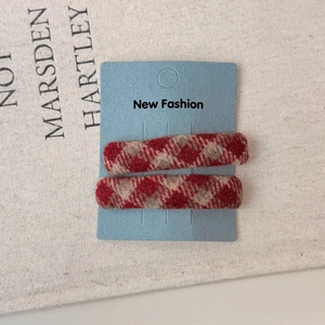 Close-up of red plaid fabric BB hair clips on a blue card against linen background
