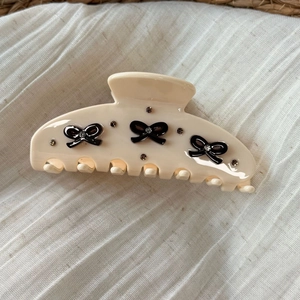 Creamy white acetate hair claw clip featuring black 3D bows and sparkling rhinestones