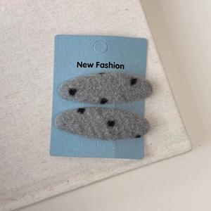 Detail of two gray felt hair clips with black polka dots on blue display card