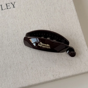 Macro detail of dark brown resin banana hair clip with elegant golden French lettering