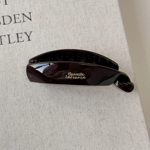 Macro detail of dark brown resin banana hair clip with elegant golden calligraphy lettering