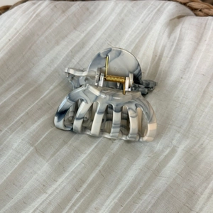 Detail showing marble-textured acetate hair claw clip with golden metal spring mechanism