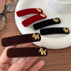 Hand holding velvet hair clips with golden dog icons in red, black and brown colors
