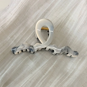 Detail of gray marble acetate hair claw clip with golden spring on textured fabric