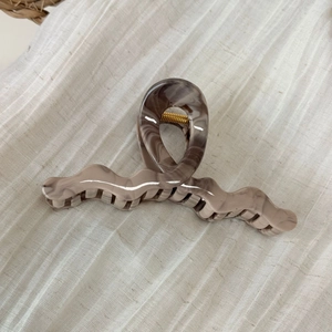 Macro detail of wave shaped marble acetate hair claw with high gloss golden metal spring