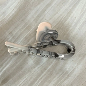 Macro shot of dark marble texture acetate hair claw clip with heart detail on linen