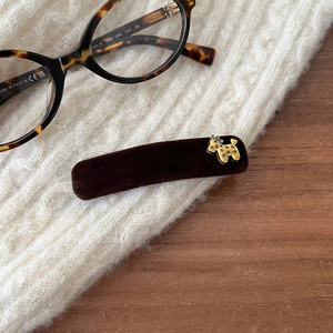 Detail of dark brown velvet hair clip with golden poodle charm on a knit sweater