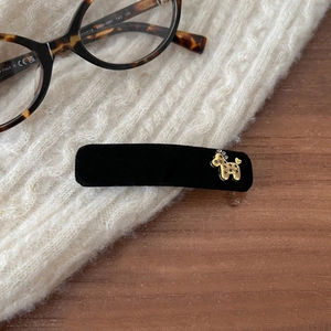Detail of a velvet BB hair clip with a gold dog emblem on a cozy white knit sweater