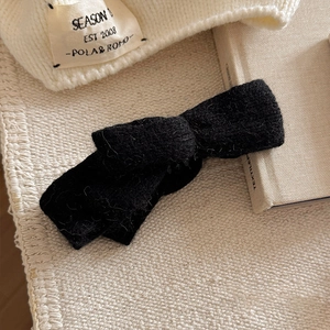 Close-up of black knitted bow hair clip on warm cream background showing winter texture