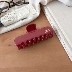 Elegant burgundy shark hair claw clip with gold lettering on a minimalist wooden desk
