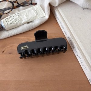 Large black polished shark hair claw with gold lettering on a stylish desk setup