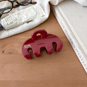 Detailed view of large dark red resin shark hair claw clip on wooden desk setting