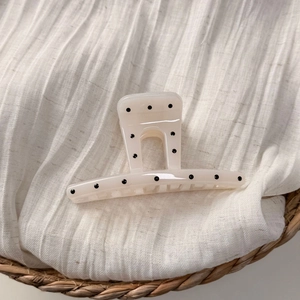 Detail der cremefarbenen Haarklammer mit schwarzen Punkten auf Stoff in einem Korb