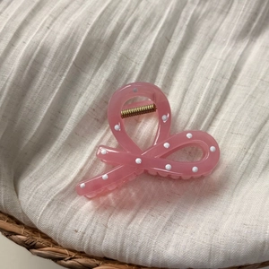 Détail de la pince à cheveux rose translucide à pois sur un tissu en coton blanc