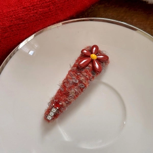 Close-up of red knit flower hair clip with pearls and rhinestones on white plate