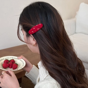 Red velvet bow hair clip with white polka dots worn by a woman with long wavy hair