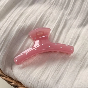 Vue détaillée d'une pince à cheveux rose à pois en résine brillante sur tissu blanc