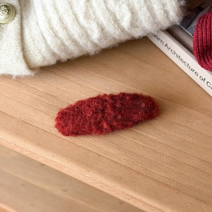 Macro detail of red fuzzy plush heart hair clip texture on a warm wooden background