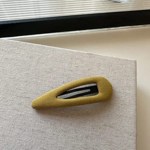 Detail of yellow plaid cotton fabric texture on a teardrop-shaped metal hair clip