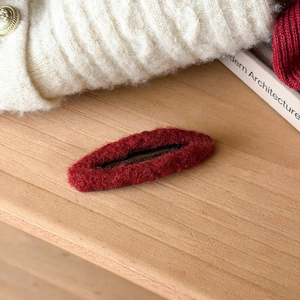 Close-up of a burgundy plush hair clip on a wooden surface with a cozy knitted background